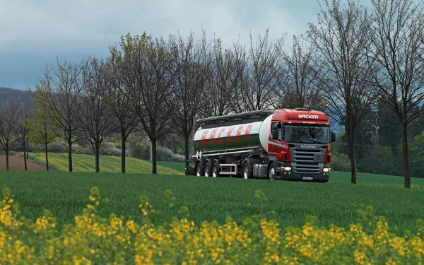 A Scania truck drives through a vibrant green field, framed by rows of trees and a backdrop of a cloudy sky, creating a striking HD desktop wallpaper.