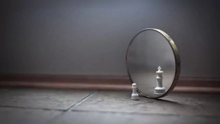 A white chess pawn stands in front of a round mirror, reflecting an image of a white queen against a soft, muted background. HD desktop wallpaper and photography.