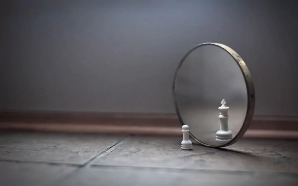 A white chess pawn stands in front of a round mirror, reflecting an image of a white queen against a soft, muted background. HD desktop wallpaper and photography.