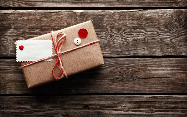 HD PC desktop wallpaper of a rustic gift wrapped in brown paper with red and white buttons, tied with red string, placed on a weathered wooden surface.
