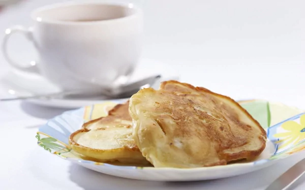 HD PC desktop wallpaper featuring a close-up of fluffy pancakes on a colorful plate with a white coffee cup blurred in the background.