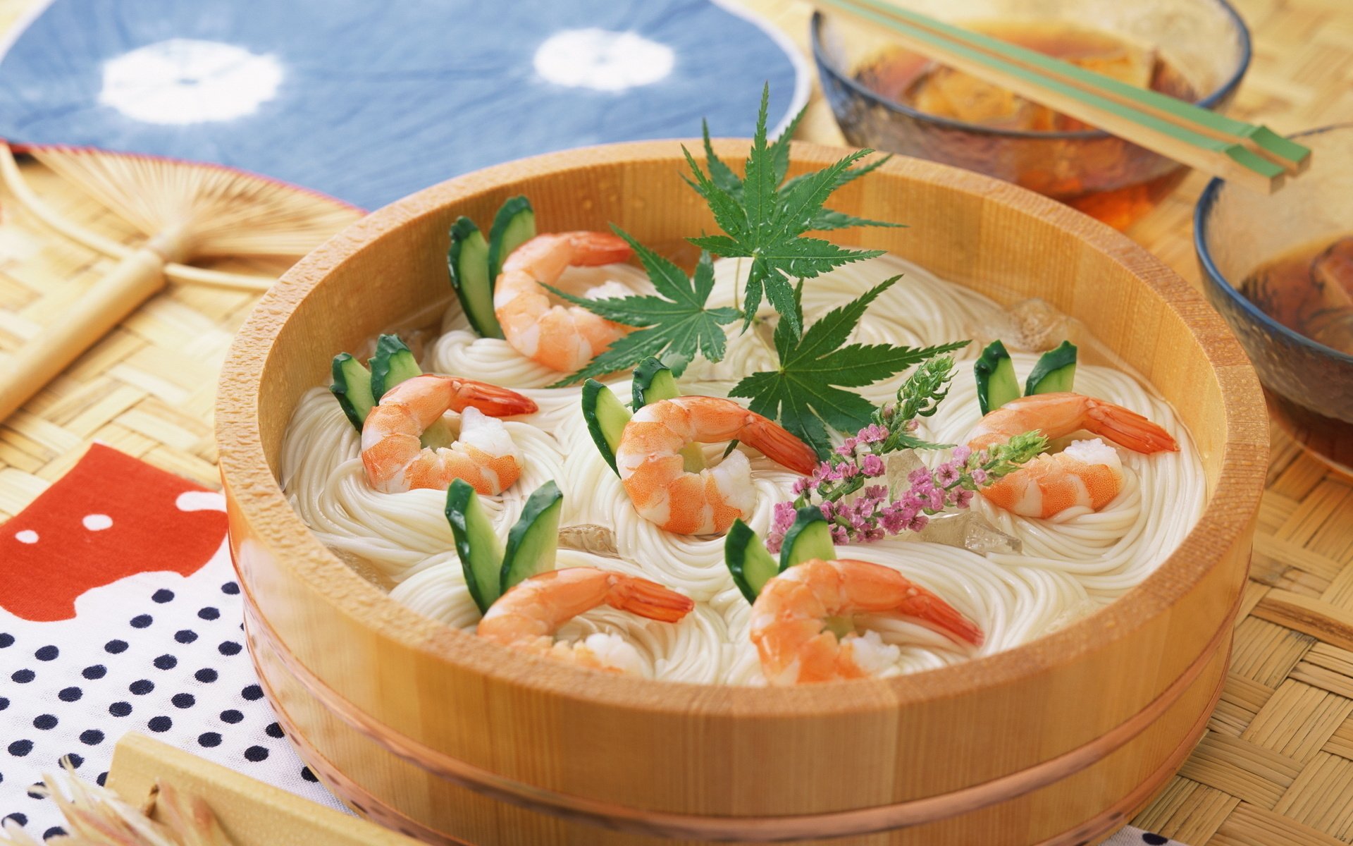 HD desktop wallpaper featuring a wooden bowl of chilled shrimp pasta garnished with green herbs, set on a traditional woven mat with chopsticks and dipping sauce.