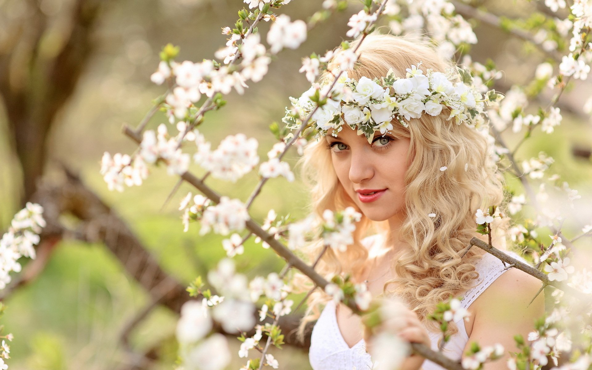 HD desktop wallpaper featuring a woman with blonde curls wearing a flower crown amidst blooming branches, evoking a tranquil mood.