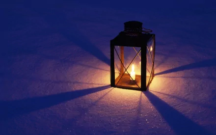 A cozy lantern emits a warm glow against a dark background, casting long shadows on the surface. This HD image serves as an inviting desktop wallpaper and background.
