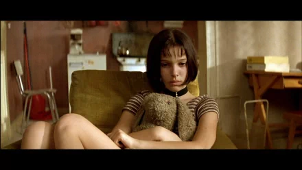 HD PC desktop wallpaper featuring a scene from the movie Leon: The Professional, showing a young girl sitting thoughtfully in a dimly lit room.