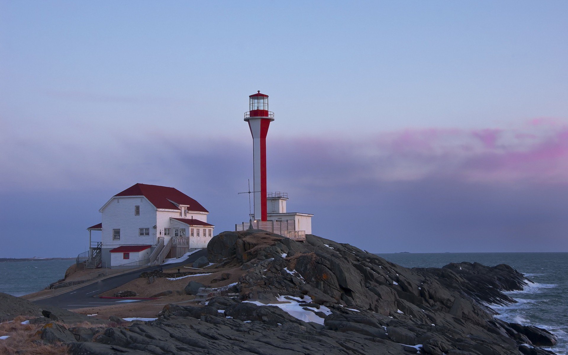 A striking lighthouse stands on rocky shores, featuring a red and white design against a serene sky, creating a captivating scene for a HD desktop wallpaper or background.