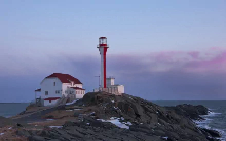 A striking lighthouse stands on rocky shores, featuring a red and white design against a serene sky, creating a captivating scene for a HD desktop wallpaper or background.