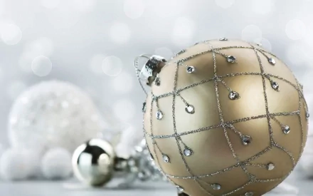 A close-up of elegant Christmas ornaments in soft focus, showcasing a golden ornament adorned with delicate shimmering details, set against a festive, blurred background.