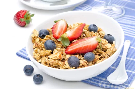 HD desktop wallpaper of a breakfast still life featuring a bowl of muesli topped with fresh strawberries and blueberries on a blue-striped cloth.