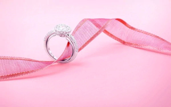 A close-up of an elegant diamond ring displayed on a soft pink background, accentuated by a delicate pink ribbon, showcasing exquisite man-made jewelry in HD detail.