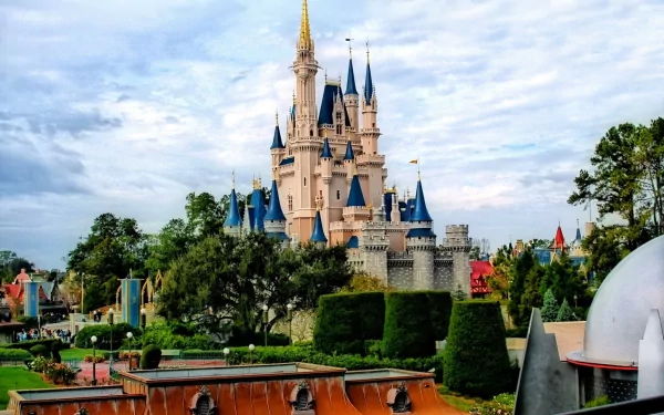 A stunning HD desktop wallpaper featuring a majestic, man-made castle with towering spires, surrounded by lush greenery and intricate landscaping under a cloudy sky.