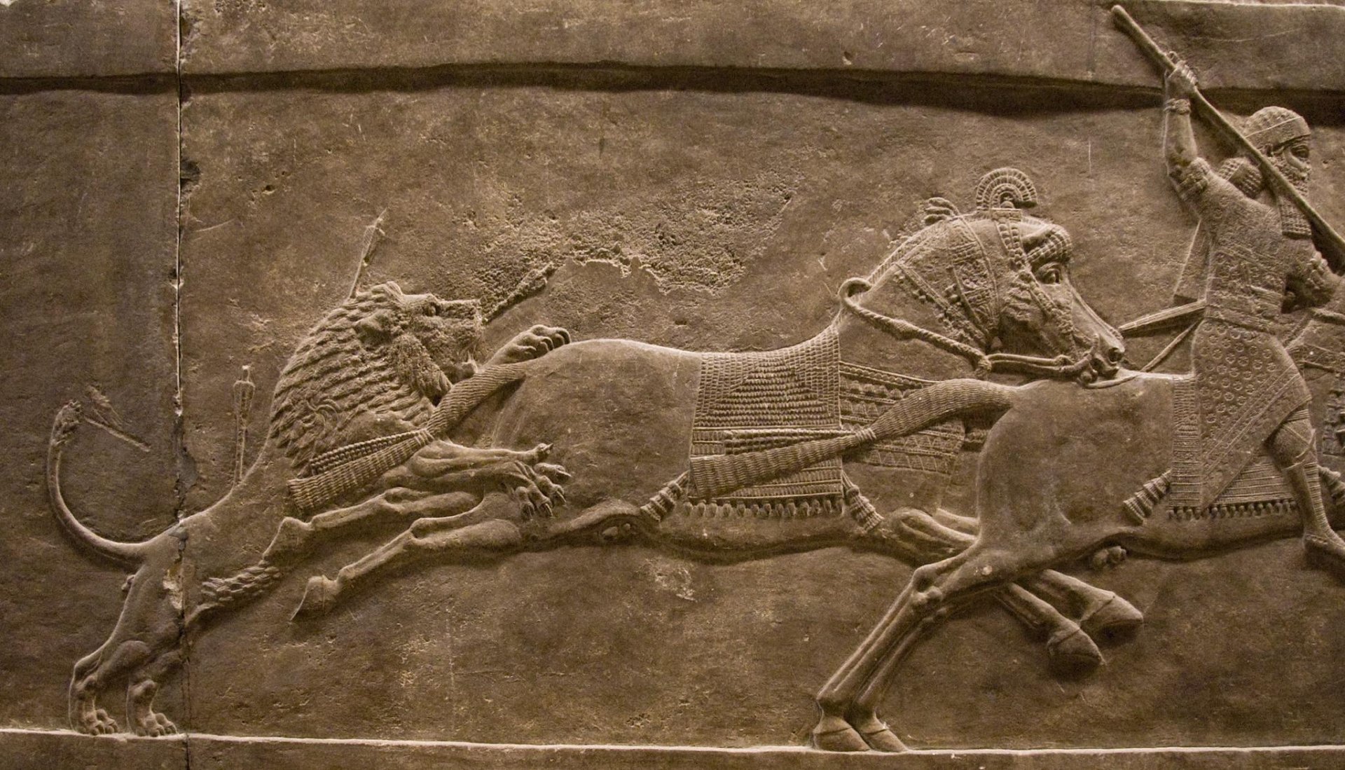 Artistic HD PC desktop wallpaper and background: Assyrian bas‑relief of a dramatic lion hunt, carved stone scene of lions leaping onto horses and chariots.