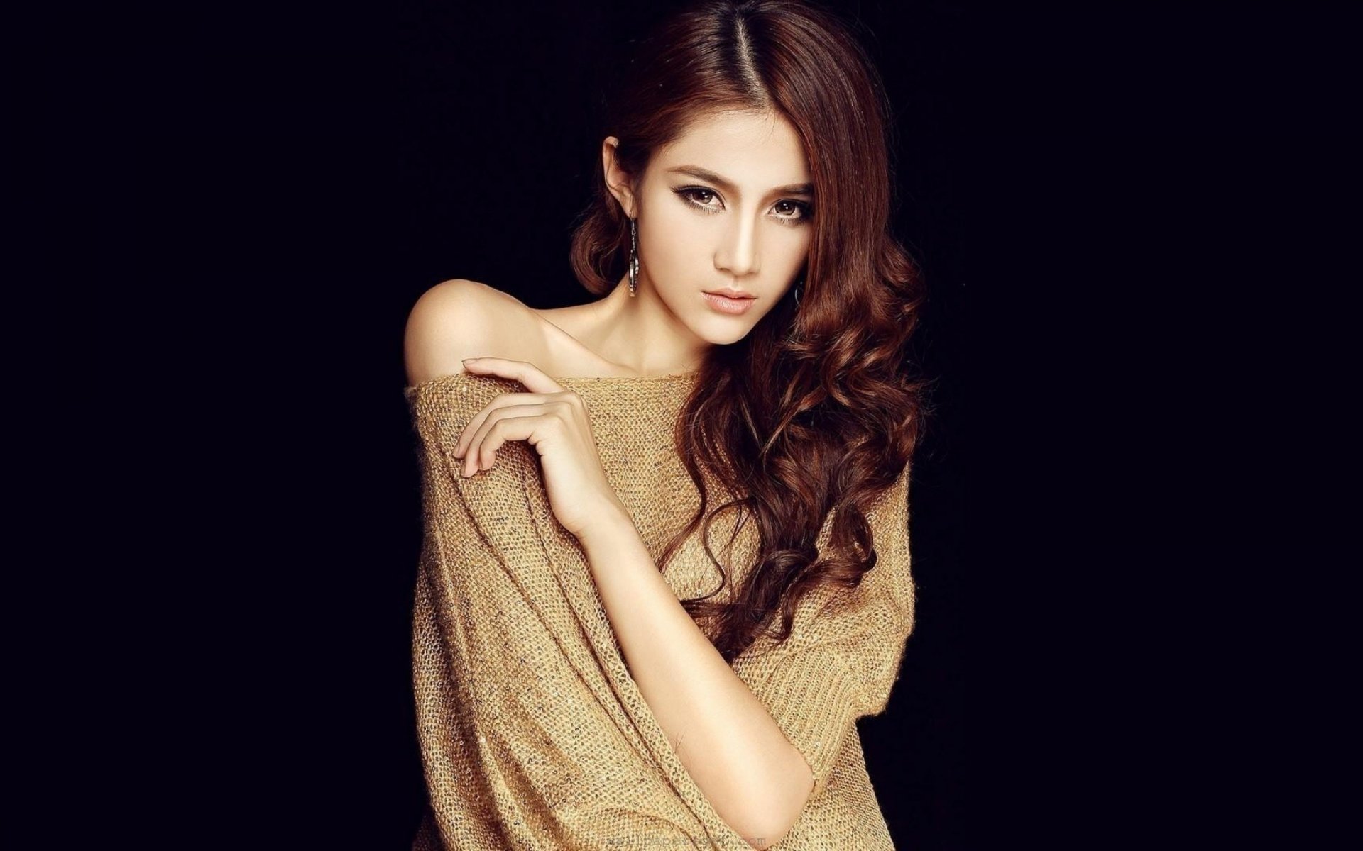A close-up of a woman with long, wavy hair, wearing a light brown sweater. This HD wallpaper features a sleek, dark background, enhancing her elegant pose and expression.
