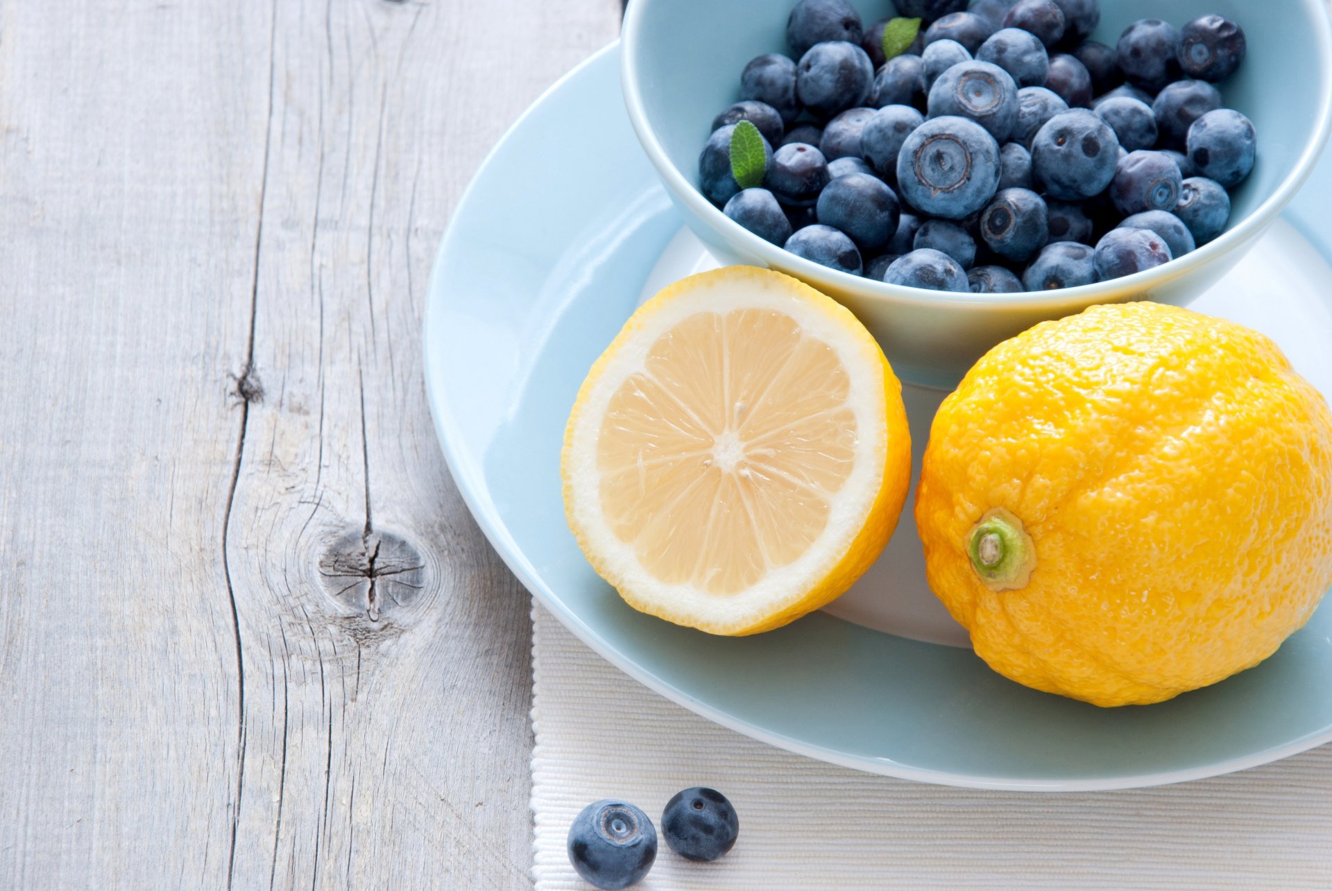 A 4K Ultra HD desktop wallpaper featuring fresh blueberries in a bowl alongside whole and halved lemons on a rustic wooden surface.