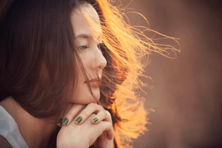 A woman with flowing hair gazes pensively, her hands gently clasped. This HD desktop wallpaper captures a serene moment infused with warm, golden light.