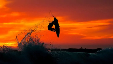 HD wallpaper: Silhouetted surfer catching air against a vibrant sunset, with waves crashing beneath. The image captures the essence of surfing and sports in a stunning evening backdrop.