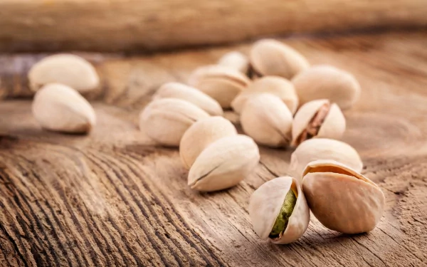 Close-up of pistachio nuts scattered on rustic wooden surface, captured in sharp detail for a 4K Ultra HD food-themed PC desktop wallpaper.