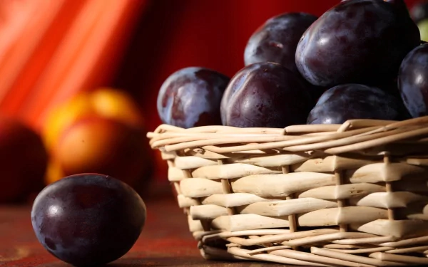 Close-up of fresh plums in a woven basket, captured in vibrant detail for a 4K Ultra HD PC desktop wallpaper and background.
