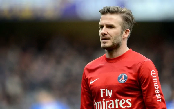 David Beckham stands on the field in a red PSG jersey, showcasing his iconic presence in sports. This HD image serves as an impressive desktop wallpaper.