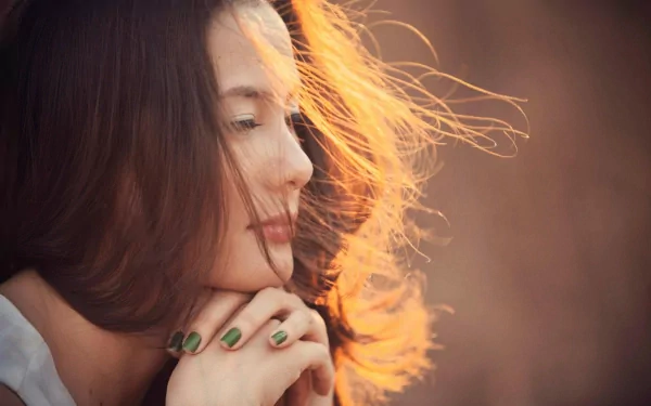 A woman with flowing hair gazes pensively, her hands gently clasped. This HD desktop wallpaper captures a serene moment infused with warm, golden light.