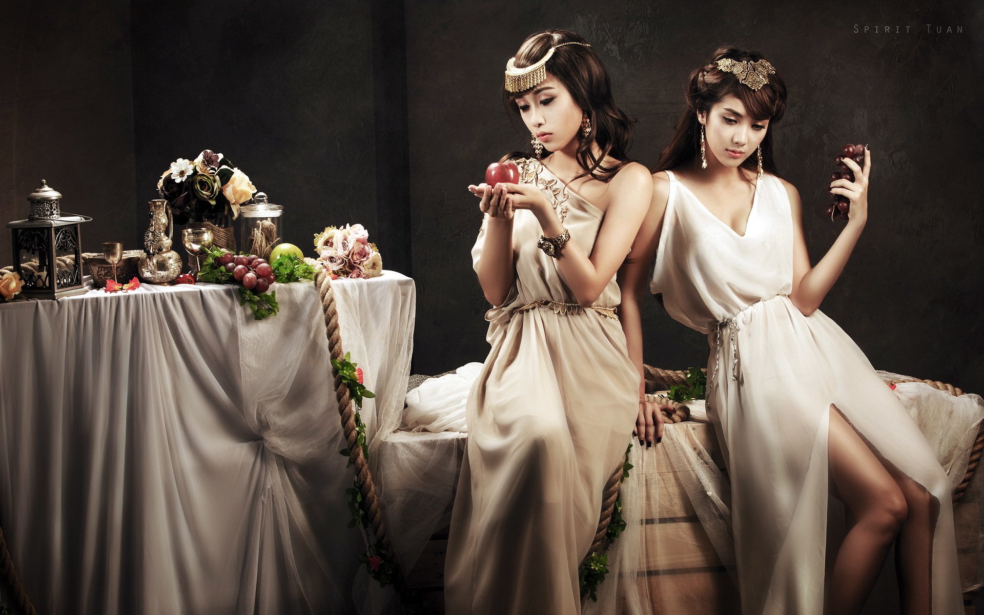A striking HD wallpaper featuring two women, Linh Napie among them, elegantly posed with fruit against a richly styled backdrop, conveying a sense of beauty and sophistication.