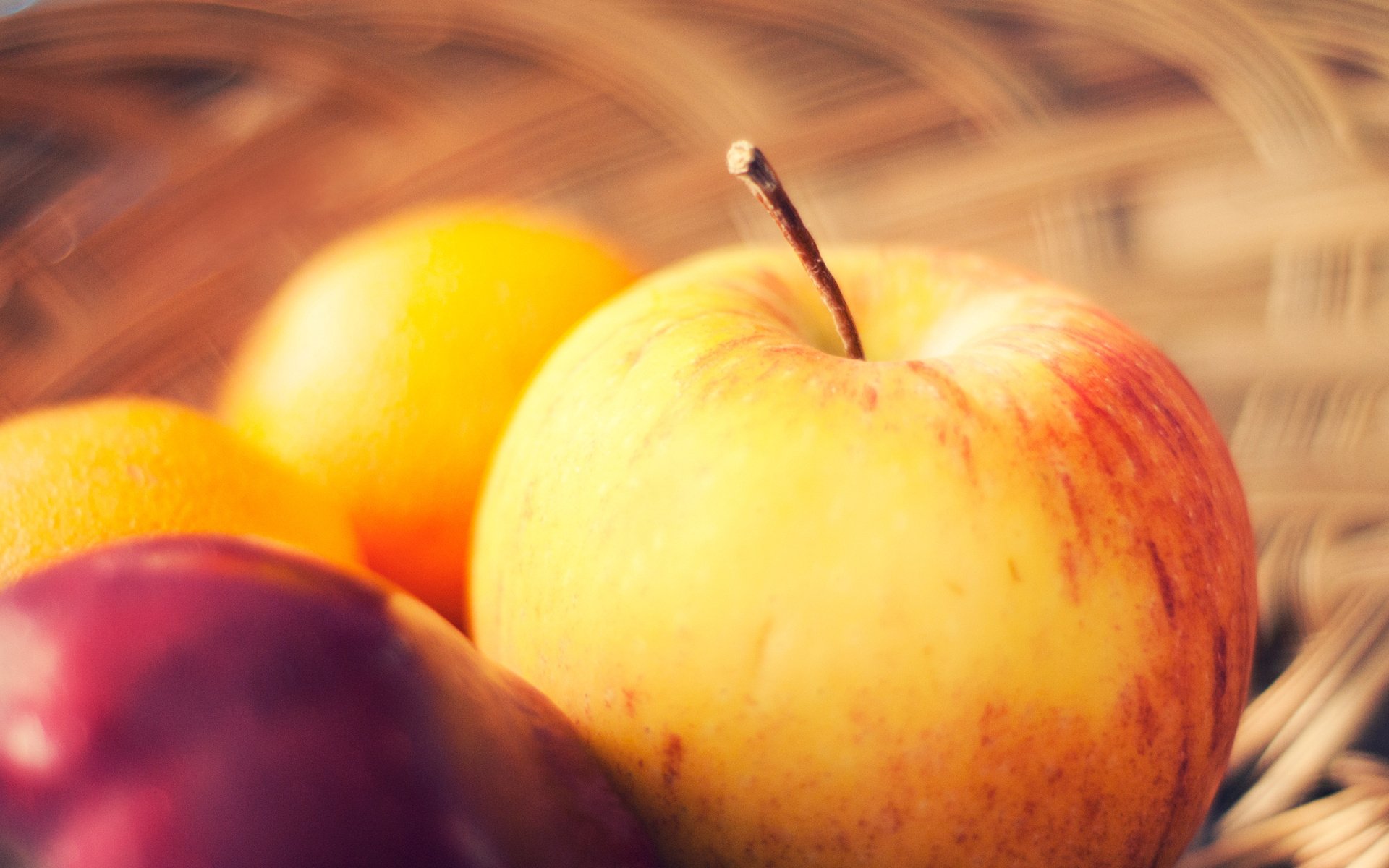 HD desktop wallpaper featuring a close-up of a yellow apple and other colorful fruits in a woven basket, highlighting fresh food in natural light.