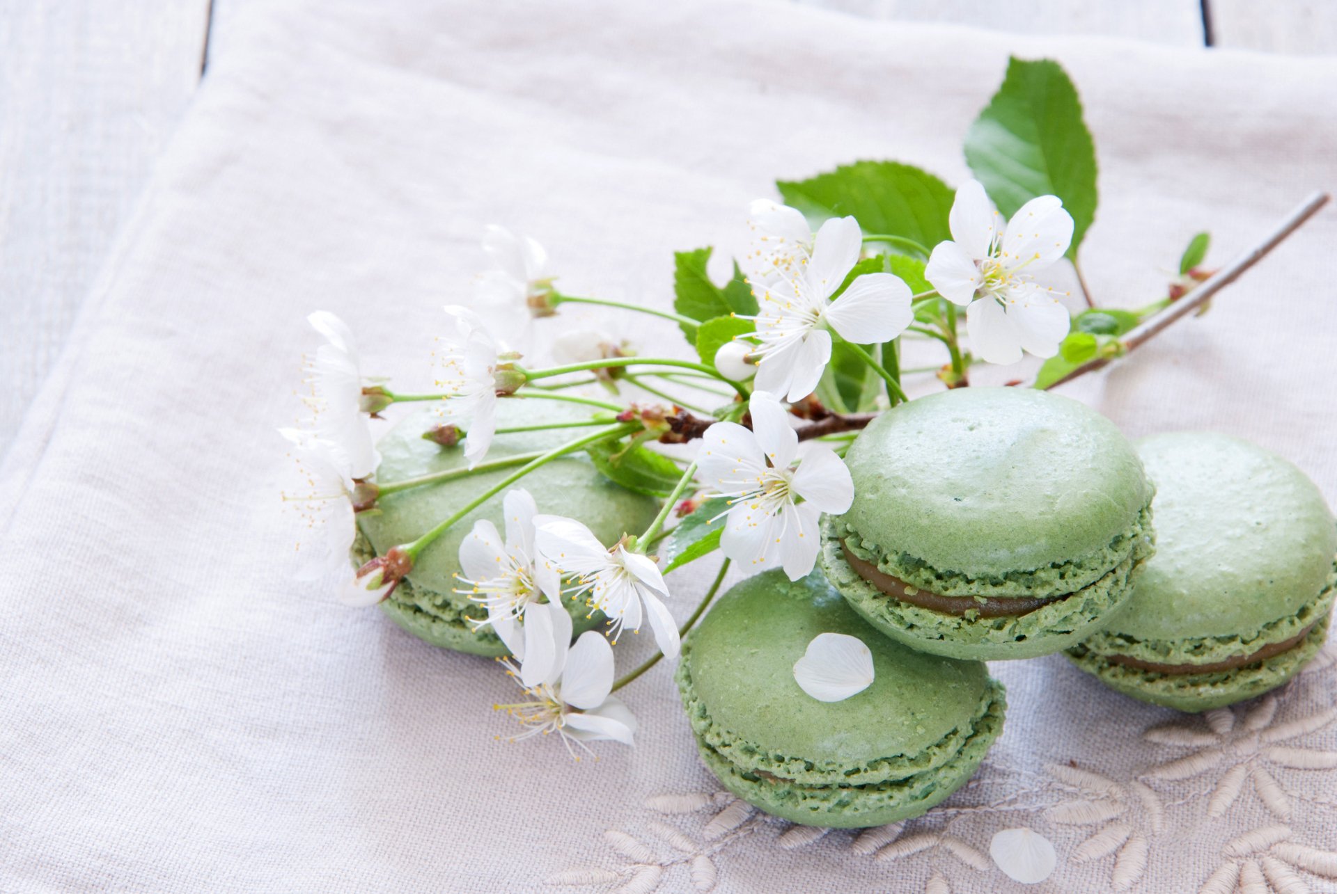 Delicate green macarons arranged with white blossoms on a soft fabric background, creating an elegant and inviting food-themed desktop wallpaper.