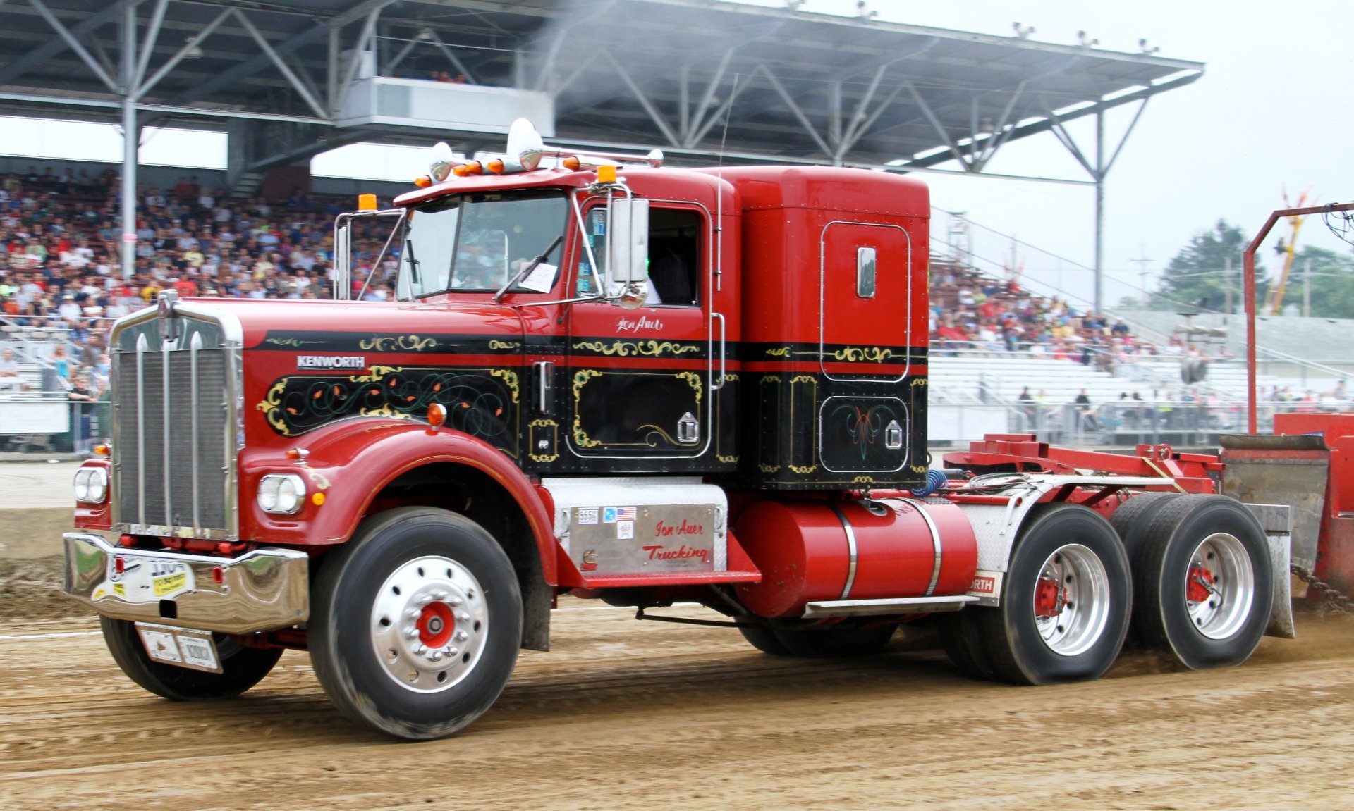 Red Kenworth tractor unit on a dirt track with grandstand crowd — 2K Quad HD PC desktop wallpaper and background.