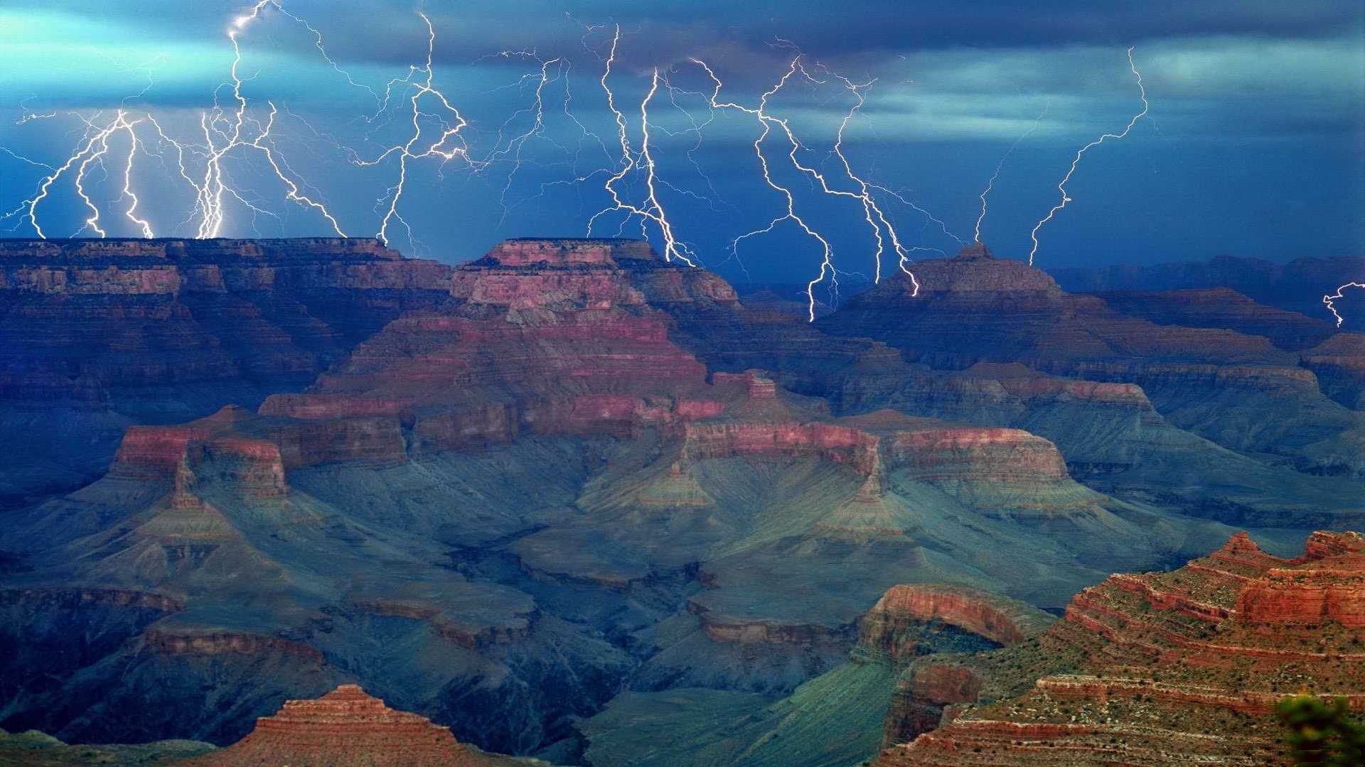 A stunning HD wallpaper of the Grand Canyon, showcasing dramatic lightning illuminating the rugged landscape against a moody sky. Nature's raw beauty captured in a moment of awe.