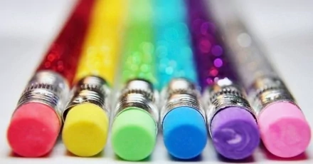 Colorful glittery pencils arranged in a vibrant spectrum, featuring capped ends in yellow, green, blue, purple, and pink, set against a blurred background. HD photography wallpaper.