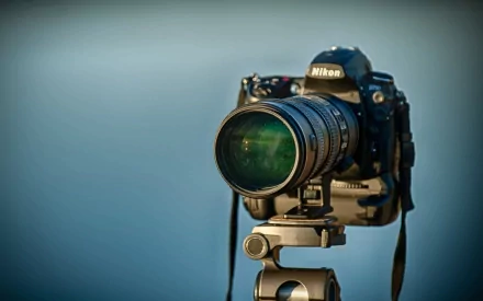A high-definition desktop wallpaper featuring a Nikon D700 camera with a lens mounted on a tripod, showcasing the blend of man-made technology and craftsmanship.