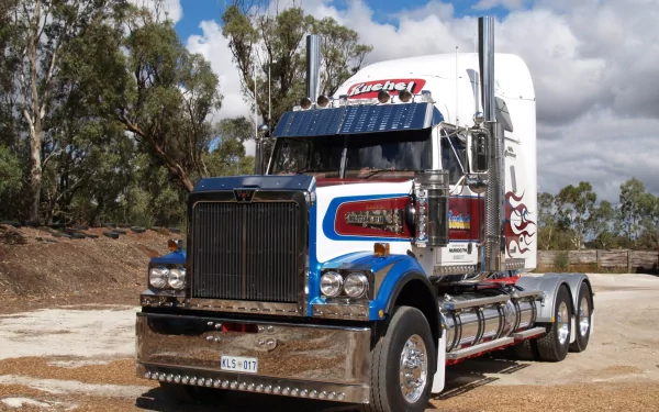 HD PC desktop wallpaper of a chrome Western Star semi-truck with blue and red accents parked on a gravel lot under a cloudy sky, framed by eucalyptus trees.