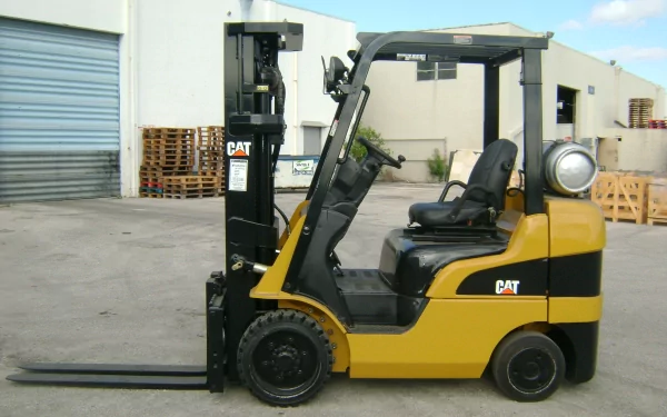 HD desktop wallpaper of a yellow Caterpillar Inc. forklift parked outdoors near a warehouse, showcasing the vehicle in clear daylight.