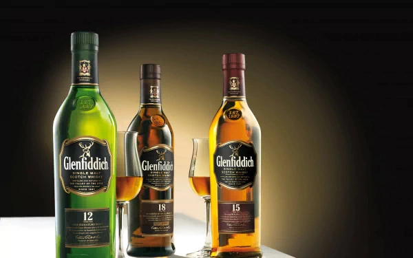 Three bottles of Glenfiddich whisky, aged 12, 15, and 18 years, displayed with glasses on a sleek surface, creating an elegant HD desktop wallpaper and background.