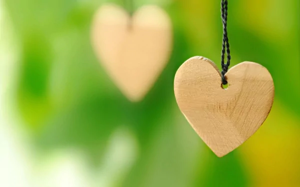 Artistic HD PC desktop wallpaper featuring two wooden heart pendants hanging against a vibrant green, softly blurred background.