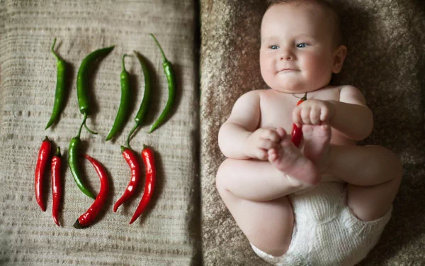 HD photography desktop wallpaper of a smiling baby lying on a textured surface next to an arrangement of red and green chili peppers.