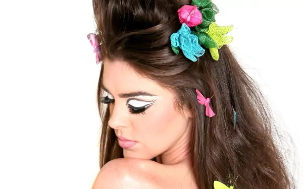 A woman with intricately styled hair adorned with colorful flowers and accessories, showcasing a striking makeup look. This image serves as a vibrant 4K Ultra HD wallpaper.