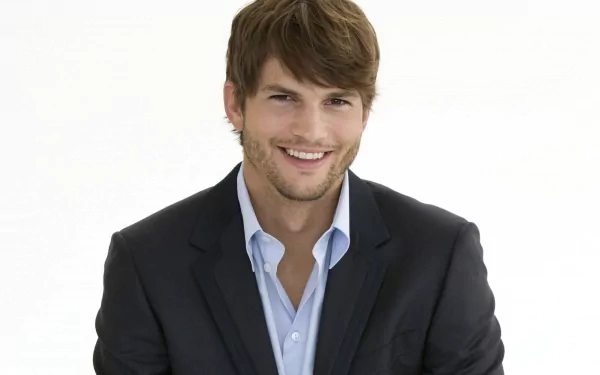HD PC desktop wallpaper featuring celebrity Ashton Kutcher in a dark suit jacket and light blue shirt, smiling against a plain white background.