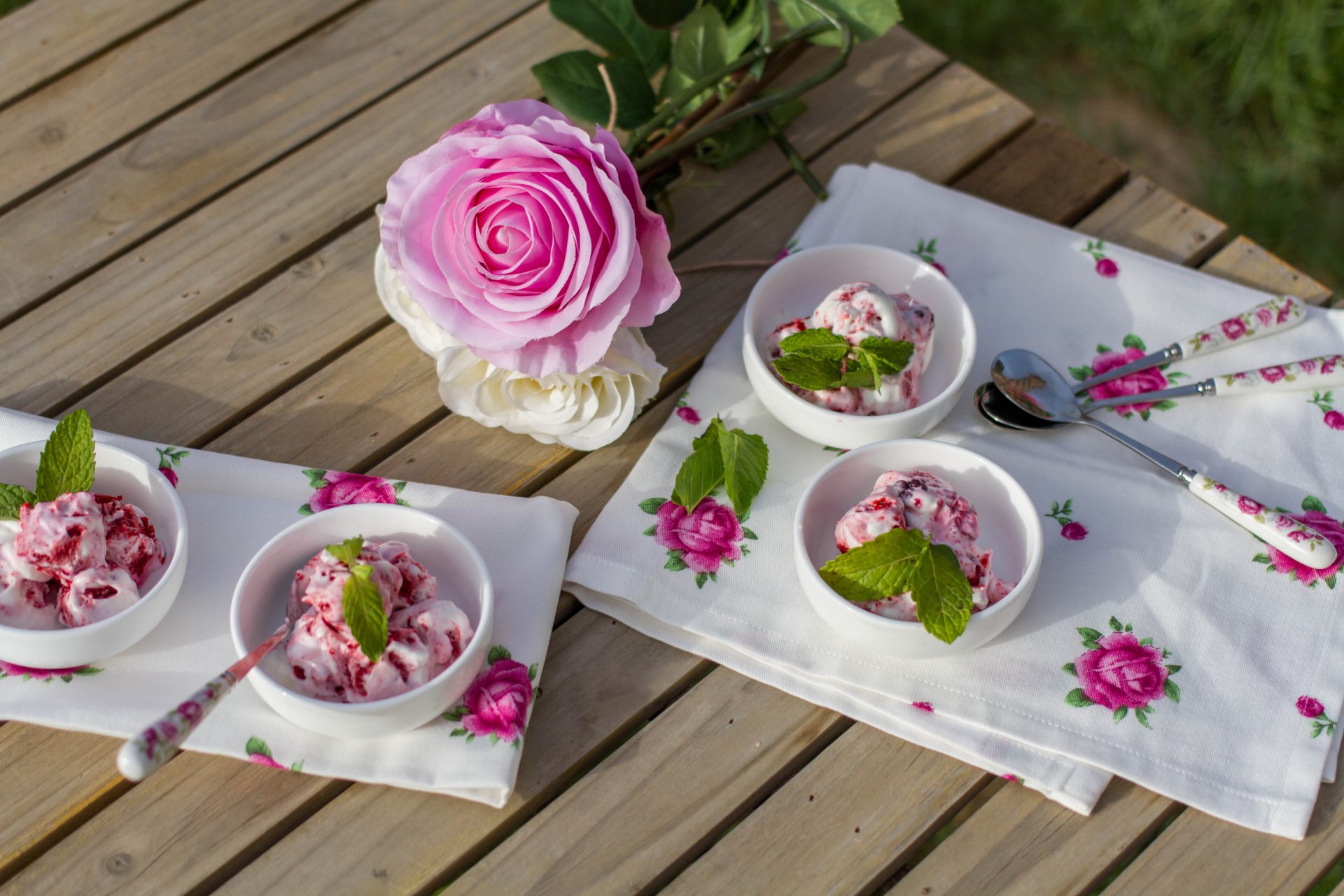 Bowls of ice cream garnished with mint leaves on a wooden table adorned with floral napkins and a pink rose. This high-definition wallpaper showcases a delightful dessert setting.