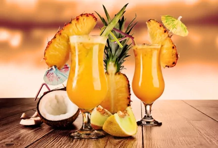 4K Ultra HD desktop wallpaper featuring vibrant tropical cocktails garnished with pineapple slices, lime, and a coconut on a wooden surface with a warm, blurred background.