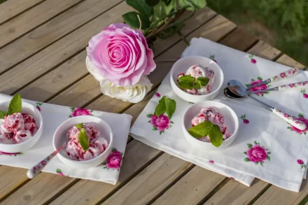 Bowls of ice cream garnished with mint leaves on a wooden table adorned with floral napkins and a pink rose. This high-definition wallpaper showcases a delightful dessert setting.
