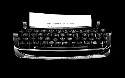 Black and white HD desktop wallpaper featuring a vintage man-made typewriter with a sheet of paper displaying Je Pense à Vous.