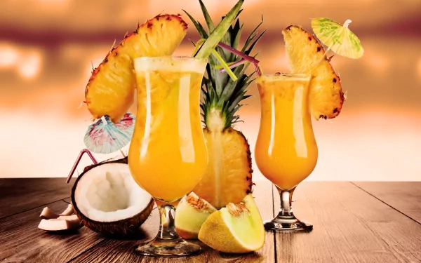 4K Ultra HD desktop wallpaper featuring vibrant tropical cocktails garnished with pineapple slices, lime, and a coconut on a wooden surface with a warm, blurred background.