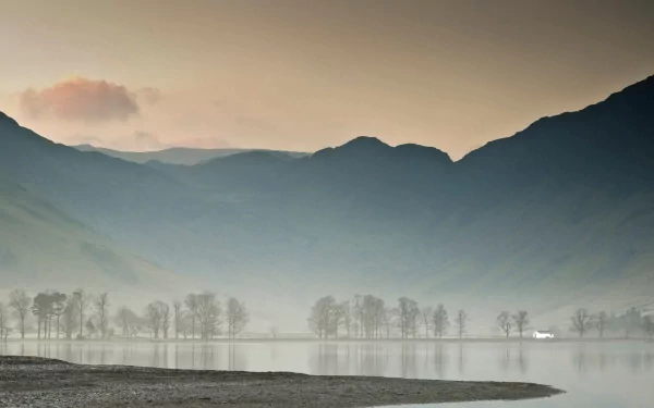A serene landscape features fog enveloping mountains and a tranquil lake, creating a peaceful nature scene. This HD wallpaper serves as an inviting desktop background.