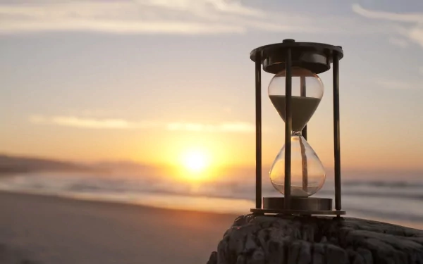 An hourglass rests on a rock, with a serene beach and sunset in the background, creating a tranquil scene for an HD PC desktop wallpaper.