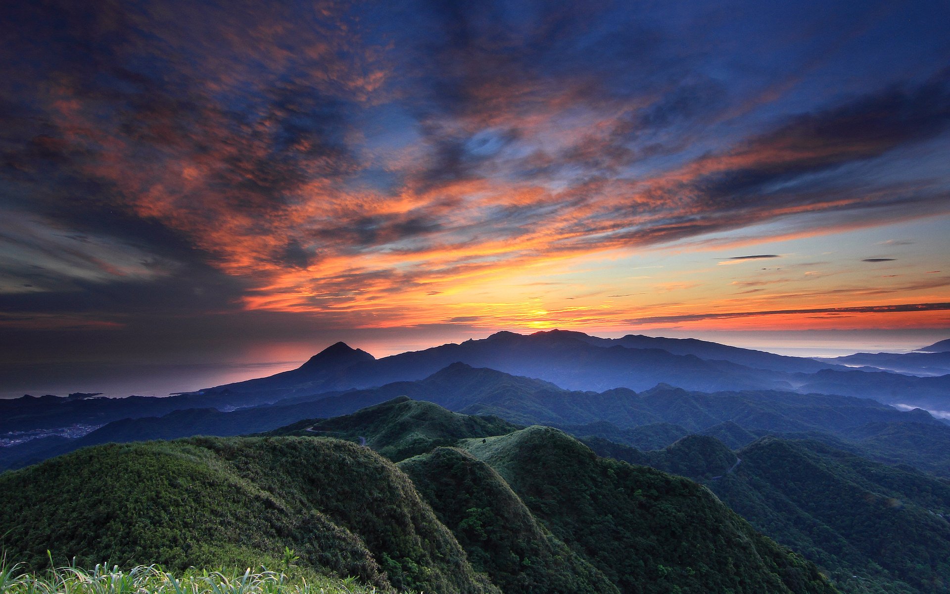 HD PC desktop wallpaper showcasing a vibrant sunset over rolling green mountains beneath a dramatic sky filled with colorful clouds.