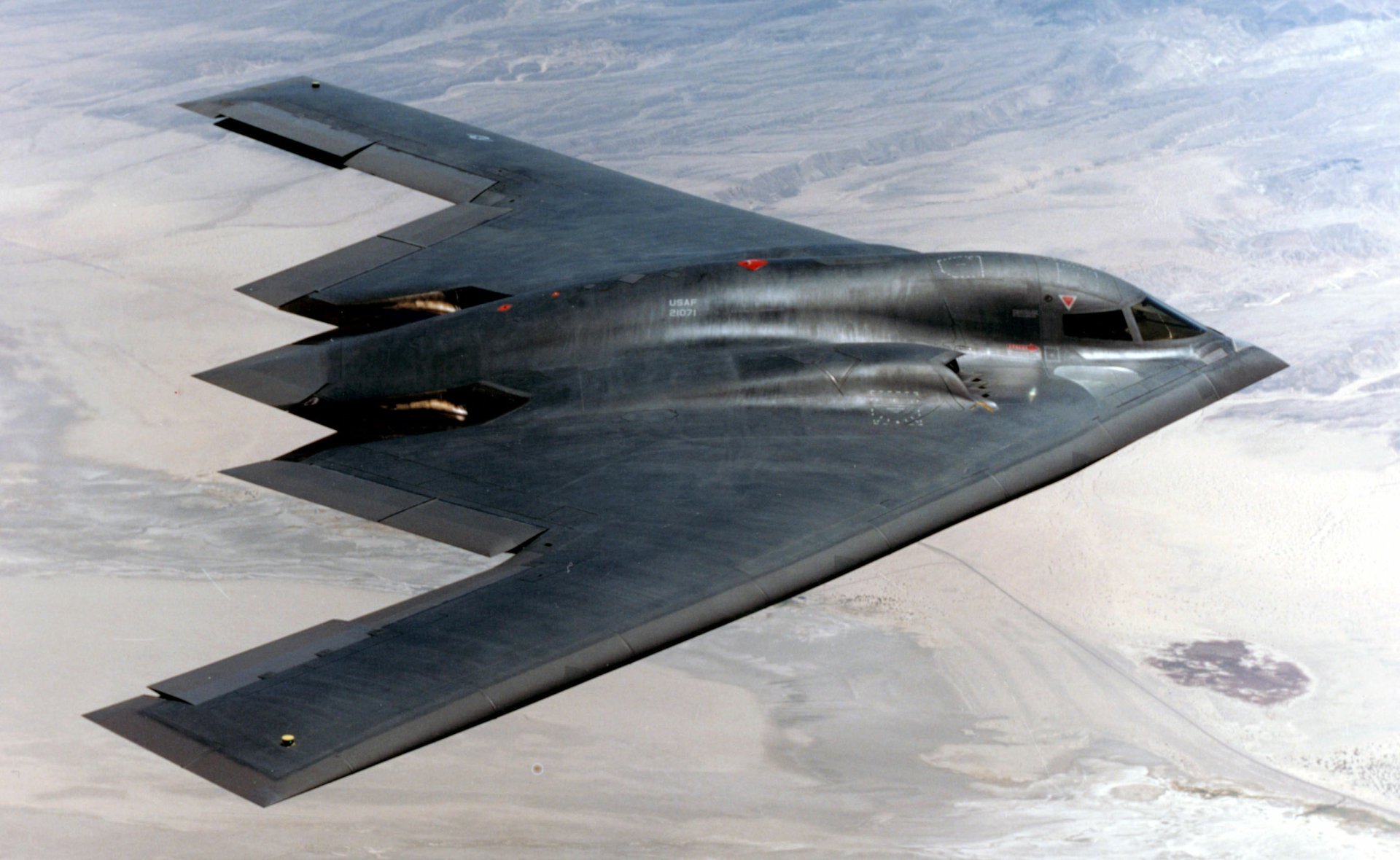 A Northrop B-2 Spirit stealth bomber flying over a desert landscape, captured in HD quality for a military-themed desktop wallpaper.