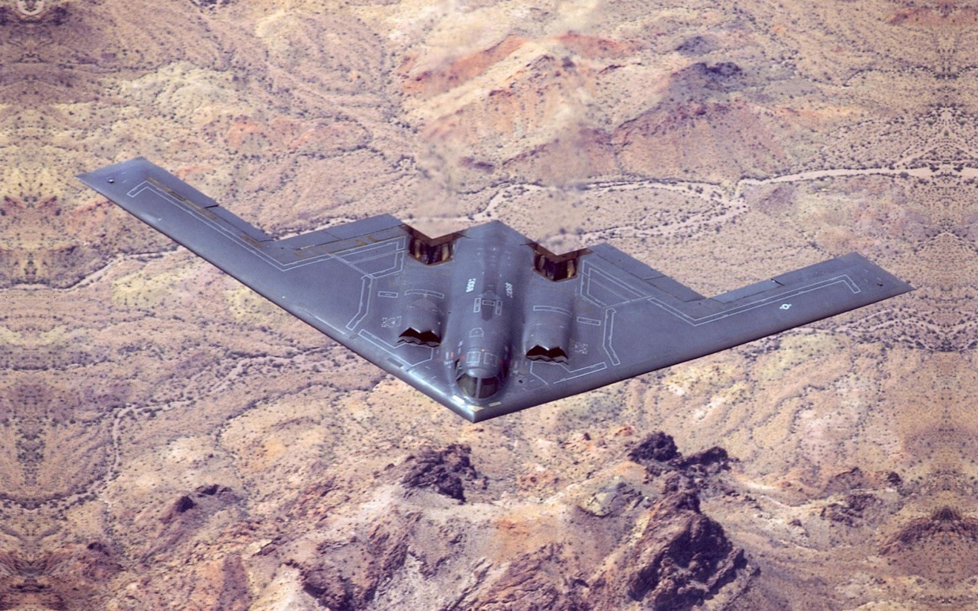 HD desktop wallpaper featuring a Northrop B-2 Spirit stealth bomber flying over rugged desert terrain, highlighting its distinctive military design and stealth capabilities.