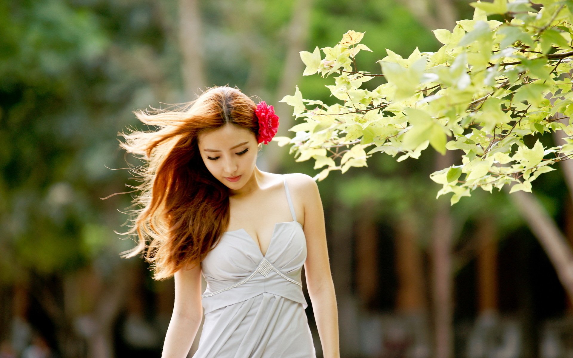 HD desktop wallpaper featuring an Asian woman with long hair and a red flower, wearing a sleeveless dress, against a serene outdoor background with green foliage.