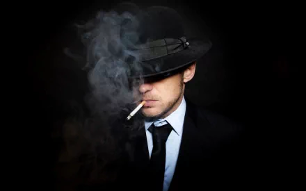 HD desktop wallpaper of a man in a suit and tie, wearing a hat that partially obscures his face. He is smoking a cigarette, with smoke swirling around, creating a moody atmosphere.